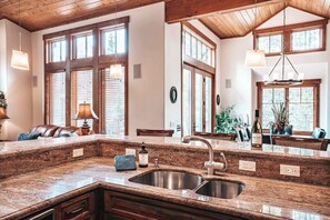 A kitchen with granite countertops, a stainless steel sink, wooden cabinets, and large windows with blinds. - Breck Connect Chalet | Gondola In/Out | Shock Hill (Breckenridge)