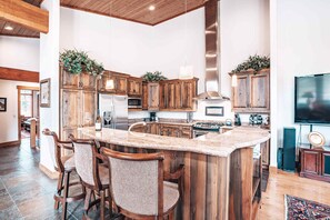 A kitchen with wooden cabinets, a central island with bar stools, and a large flat-screen TV.
