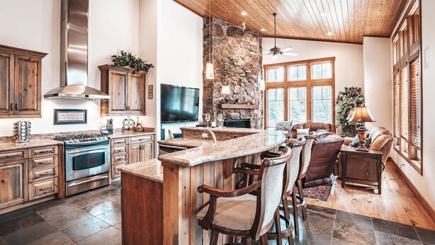 Una cocina amplia con pared de piedra, armarios de madera, una estufa grande y una zona de bar con sillas.