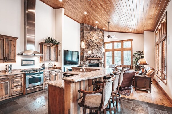 Une cuisine spacieuse avec un mur en pierre, des armoires en bois, une grande cuisinière et un coin bar avec des chaises.