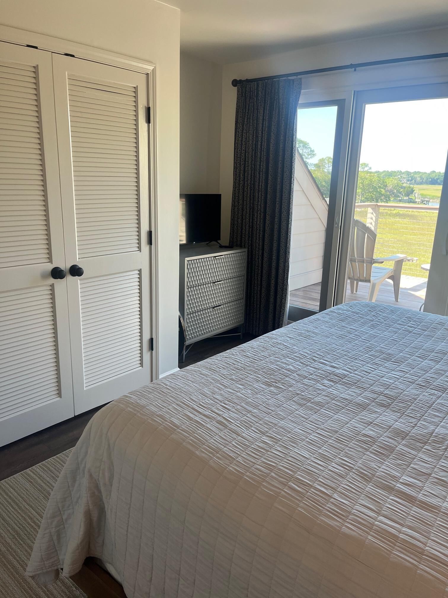 Une chambre à coucher comprenant un lit, une commode, un téléviseur et une porte-fenêtre coulissante donnant sur un balcon.