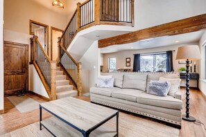 Un salon spacieux avec un escalier, un canapé, une table basse et une lampe.