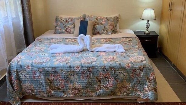 A neatly made bed with a floral bedspread, a decorative wall hanging, and a bedside lamp.