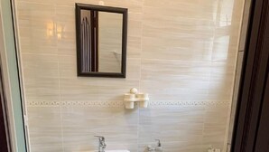 A bathroom with a white sink, a mirror, and a toilet. There are two green rugs on the floor.