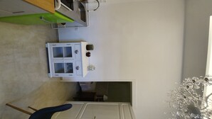 Een kleine keuken met een spoelbak, fornuis en een klein kastje. Er staat een groene stoel en er hangt een decoratieve glazen kroonluchter.