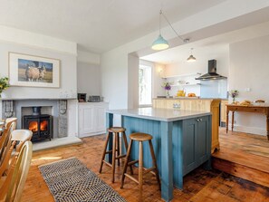 Une cuisine moderne dotée d’un îlot central, de tabourets de bar, d’une cheminée et d’un coin repas avec des chaises en bois.