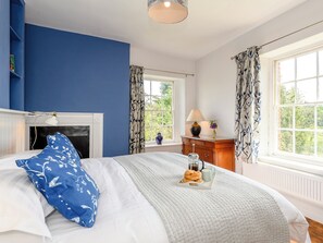 A bedroom with a bed, a dresser, a window with curtains, a fireplace, and a tray with pastries and a cup.