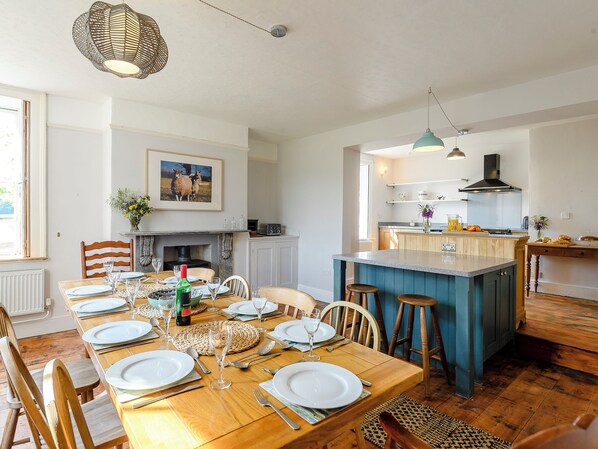 A dining area with a wooden table set for a meal, a kitchen with a blue island, and a fireplace.