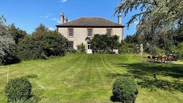 A large stone building with a tiled roof, surrounded by a well-maintained lawn and trees.
