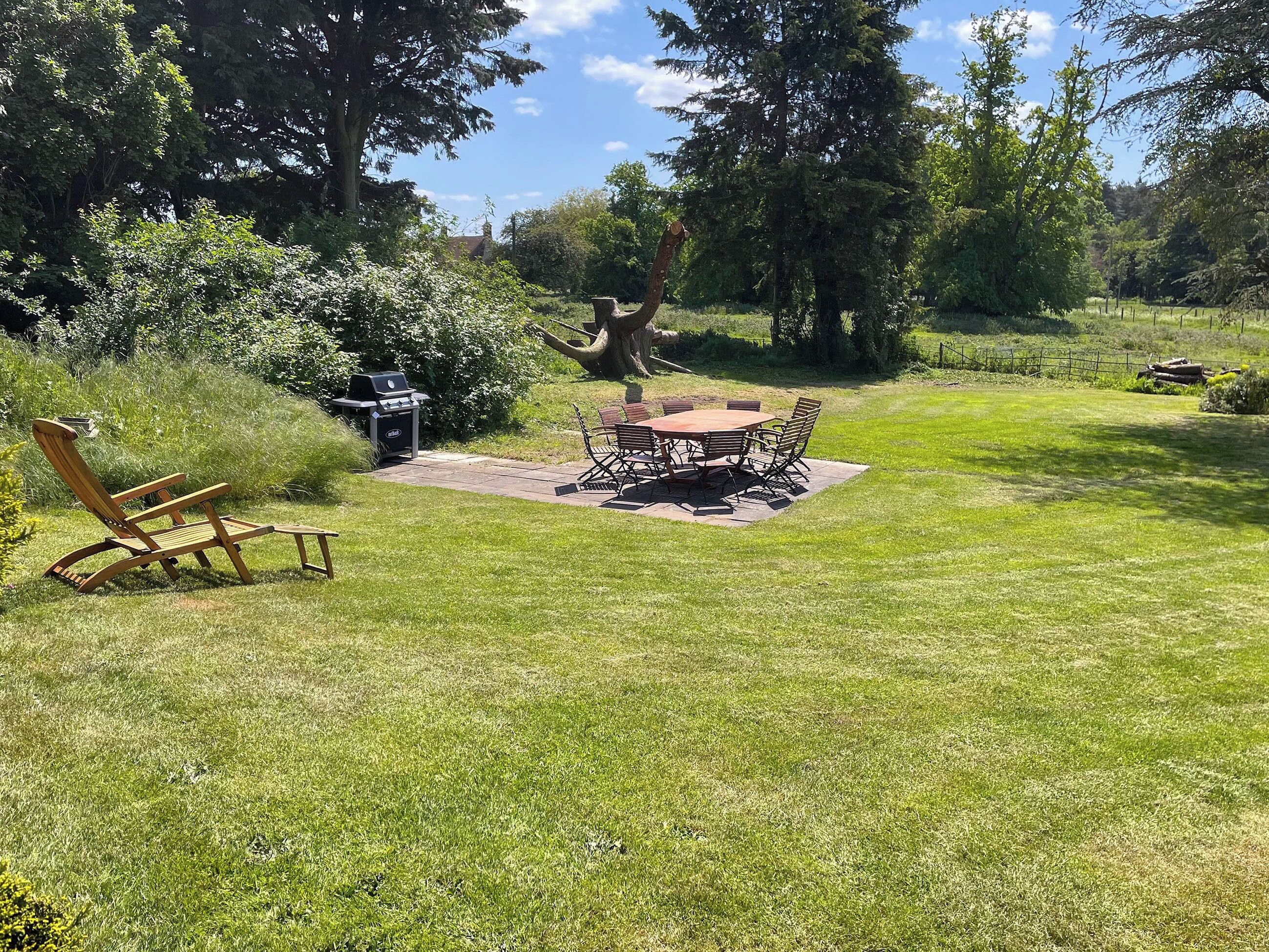 A backyard with a barbecue grill, a dining table with chairs, and a wooden chair.