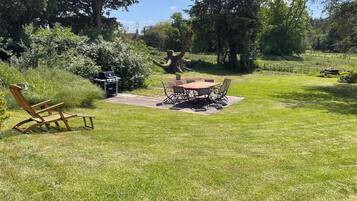 A backyard with a barbecue grill, a dining table with chairs, and a wooden chair.