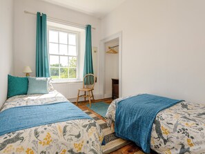 Un dormitorio con dos camas, una ventana con cortinas, una silla y un armario.