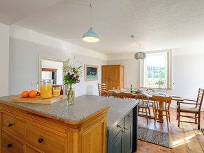 Une cuisine dotée d’un plan de travail en granit, de meubles en bois, d’un coin repas avec une table et des chaises, et offrant une vue sur l’extérieur grâce à une fenêtre.