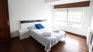 Une chambre à coucher avec un lit, une table de chevet, une fenêtre avec des stores et une porte en bois.