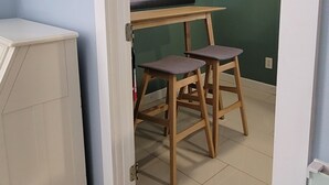 Une pièce avec un plancher en bois, un radiateur blanc, une chaise en bois, une fenêtre avec un rideau léger et un tableau encadré accroché au mur.