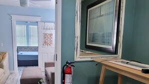 Une pièce aux murs de couleur turquoise, avec un plancher en bois, un ventilateur de plafond, une fenêtre ornée d’un cadre et un extincteur.