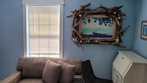 Une pièce avec une fenêtre, un canapé, une chaise, une commode et un tableau encadré au mur.
