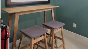 Une pièce aux murs de couleur turquoise, avec un tableau encadré, une table en bois, deux tabourets et un luminaire au plafond.