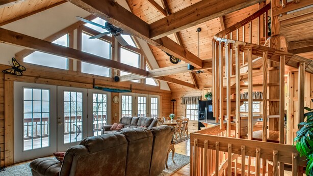 Een ruime woonkamer met een grote hoekbank, houten balken en grote ramen.