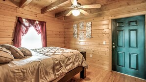 Een slaapkamer in een houten blokhut, met een bed, een plafondventilator en een blauwe deur.