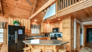 Een houten keuken in blokhutstijl met een centraal eiland, barkrukken, een koelkast en een magnetron.