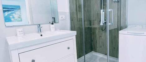 A modern bathroom with a glass-enclosed shower, a white vanity with drawers, and a large mirror.