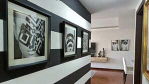A hallway with black and white striped walls, framed artwork, a wooden floor, and a dining area with a chair and table. - Apartment 3Beds + QueenBed + Balcony + Parking - 6thFLOOR (Quito)