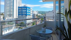 A balcony with a glass table and chairs, overlooking a cityscape with modern buildings. - Apartment 3Beds + QueenBed + Balcony + Parking - 6thFLOOR (Quito)