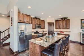 A modern kitchen with wooden cabinets, stainless steel appliances, a granite countertop, and a bar area with stools.