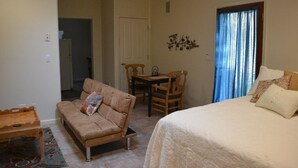 Een kamer met een bed, een slaapbank, een eettafel met stoelen, een klein houten tafeltje en een kamerkleed met dessin.