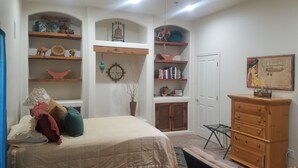 Een slaapkamer met een bed, een kast, planken met boeken, een klok en een deur.