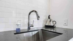 Una cocina moderna con un lavamanos de acero inoxidable, una tetera y un vaso de agua sobre la encimera.