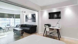 Habitación de hotel moderna con una cama grande, un escritorio con silla, un televisor de pantalla plana en la pared y un separador de vidrio que divide la habitación de un balcón.