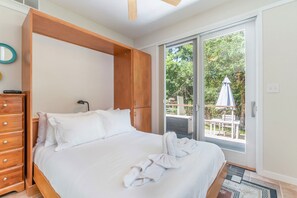 Un dormitorio con cama, armario de madera y puerta corrediza de vidrio que da a un área exterior con mesa y sombrilla.