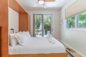 Un dormitorio con cama, ventilador de techo, ventana con persianas y puerta que da a un espacio exterior.