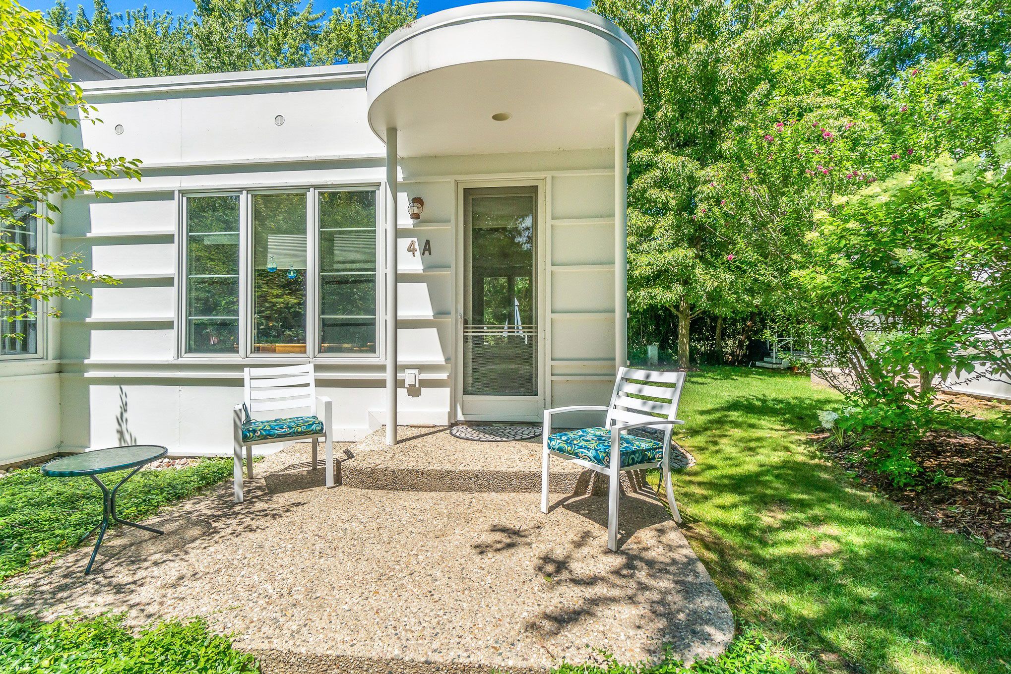 Ein Haus mit überdachter Veranda, zwei weißen Stühlen, einem kleinen Tisch und einer Tür mit der Nummer 4A.