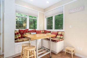 Cocina en esquina con una mesa de madera, taburetes de bar y un banco con cojines de cuadros.