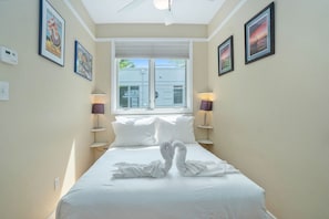 A hotel room with a bed, two bedside lamps, a window with blinds, and framed artwork on the walls.