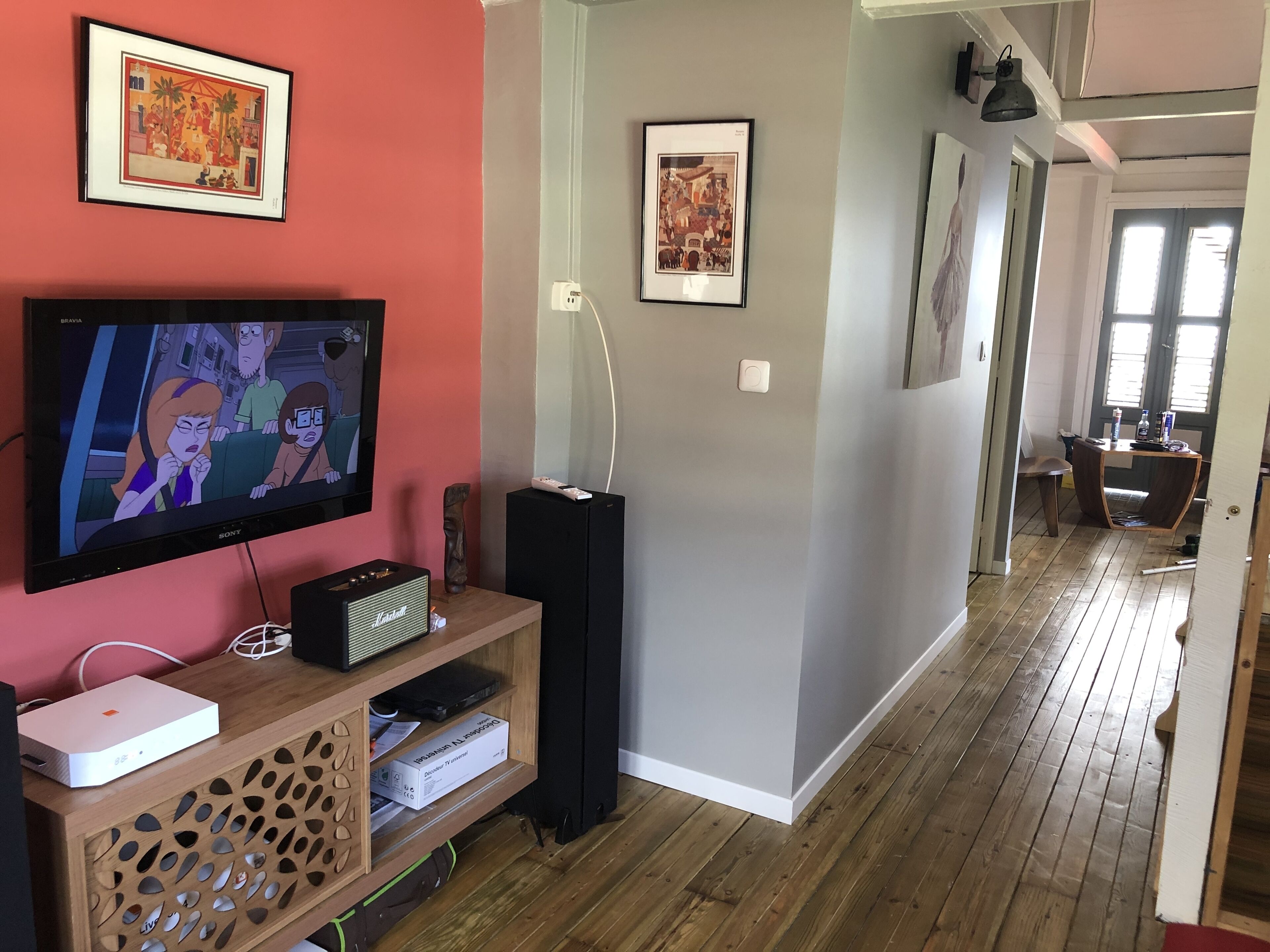 Un salon doté d’un téléviseur à écran plat, d’un meuble de rangement en bois et d’œuvres d’art encadrées accrochées aux murs.