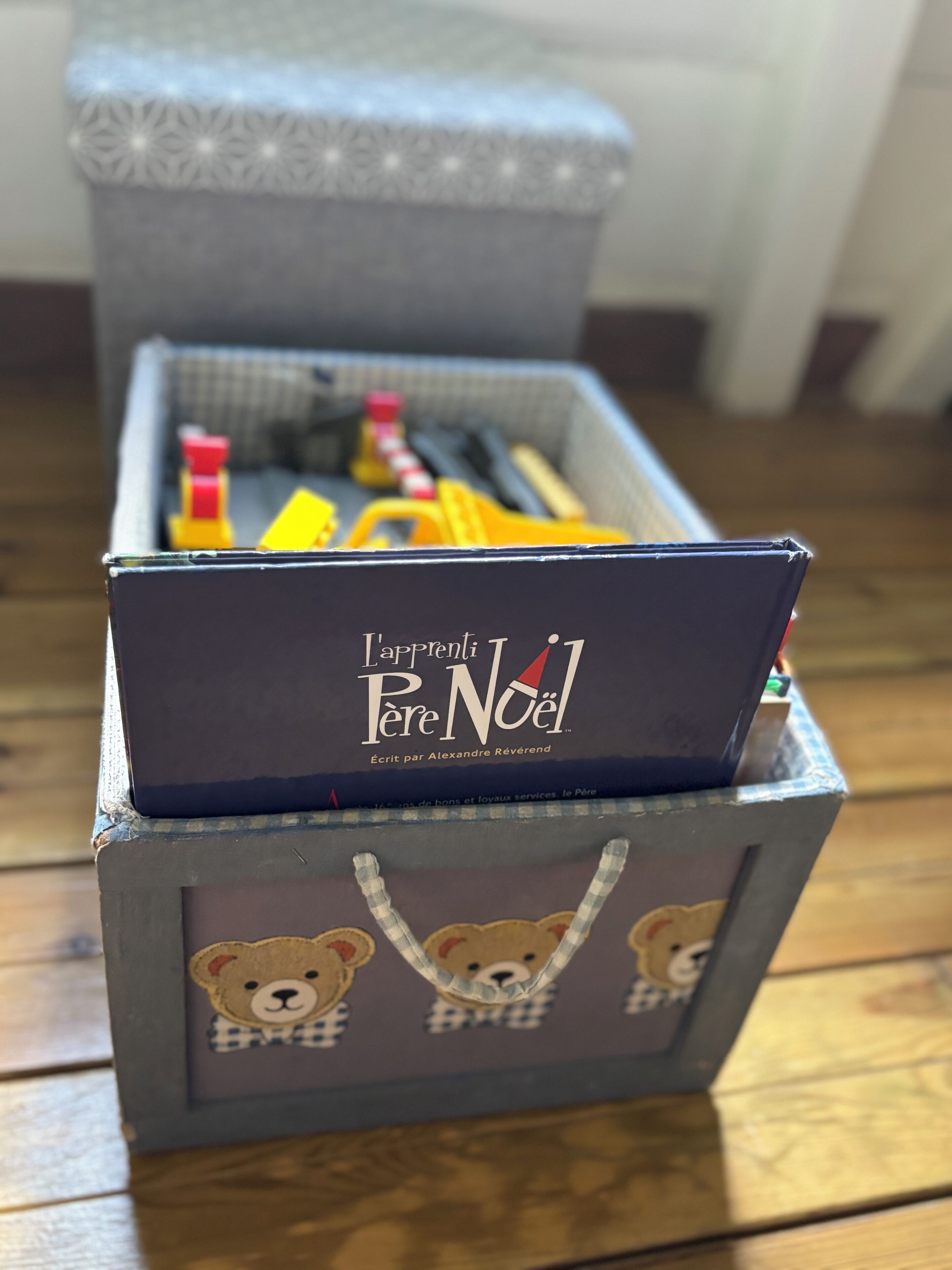 Una caja de almacenamiento con un libro titulado 'L'Appreti Père Noël' de Alexandre Réverend. La caja tiene un diseño de oso en un lateral.
