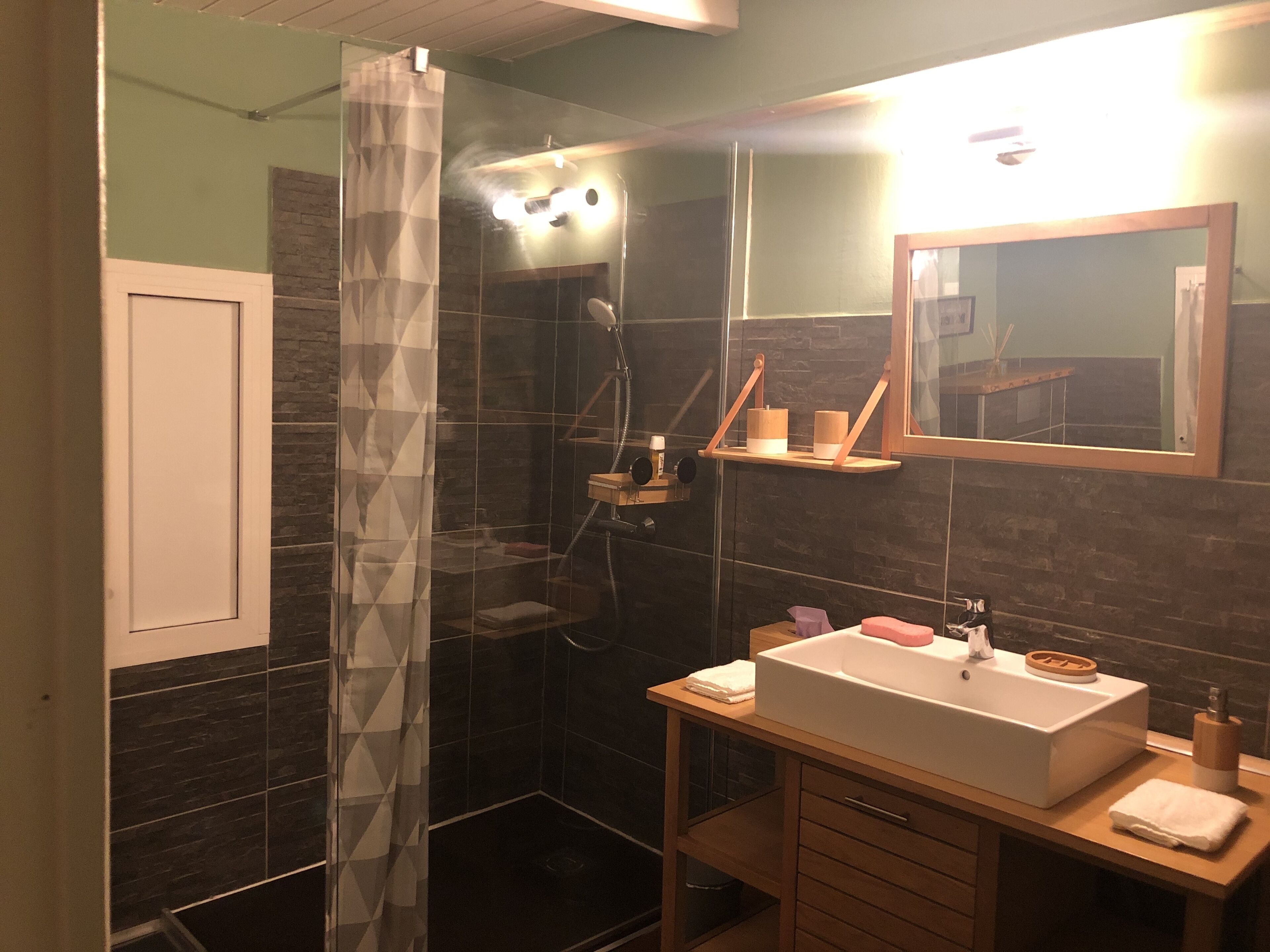 Un baño moderno con cabina de ducha de vidrio, tocador de madera y espejo sobre el lavabo.