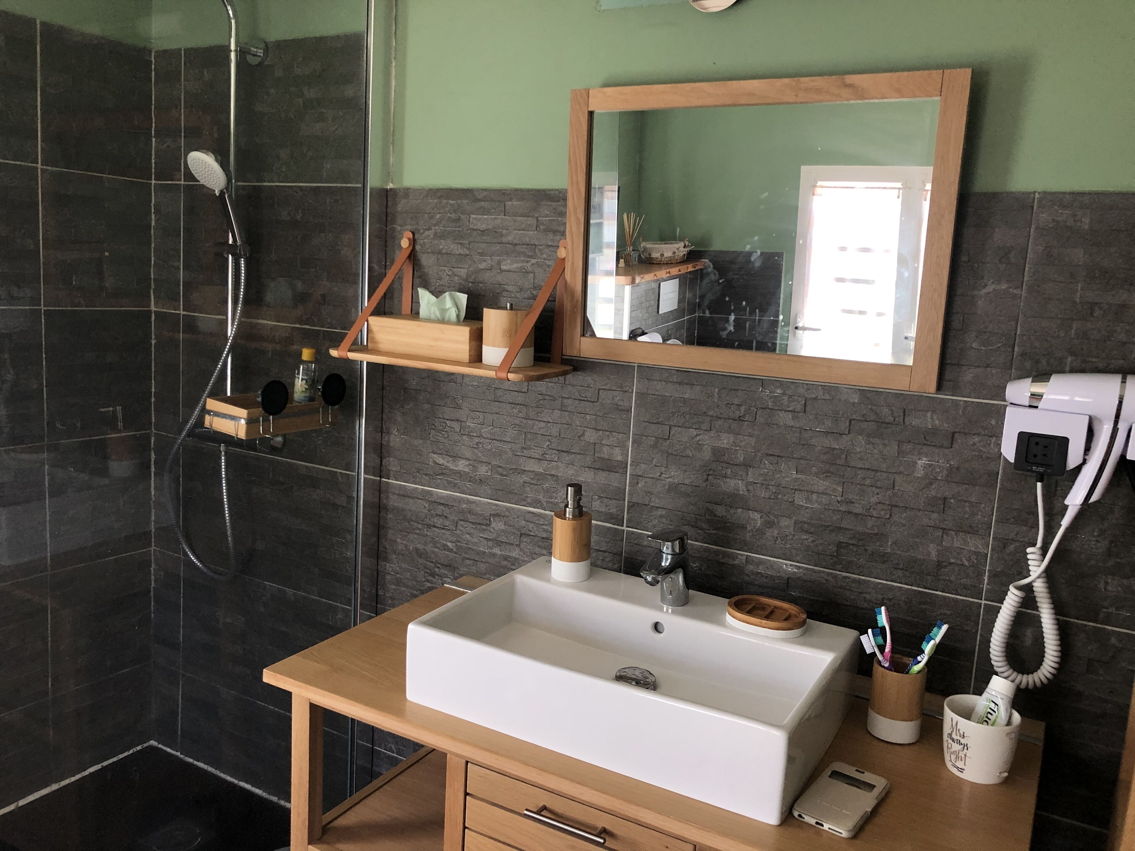 Ein Badezimmer mit einem Holzlagerfläschchen, einem weißen Waschbecken, einem Spiegel und einer Duschkabine.