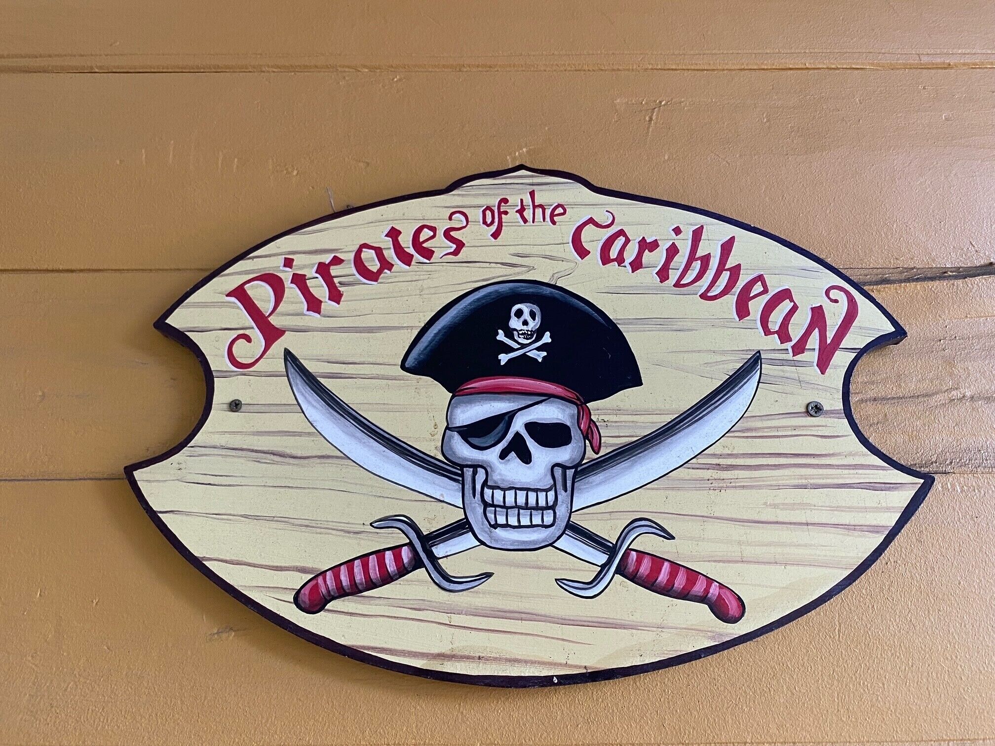 Uma placa de madeira com tema de pirata, exibindo um crânio e espadas cruzadas, e o texto 'Pirates of the Caribbean'.