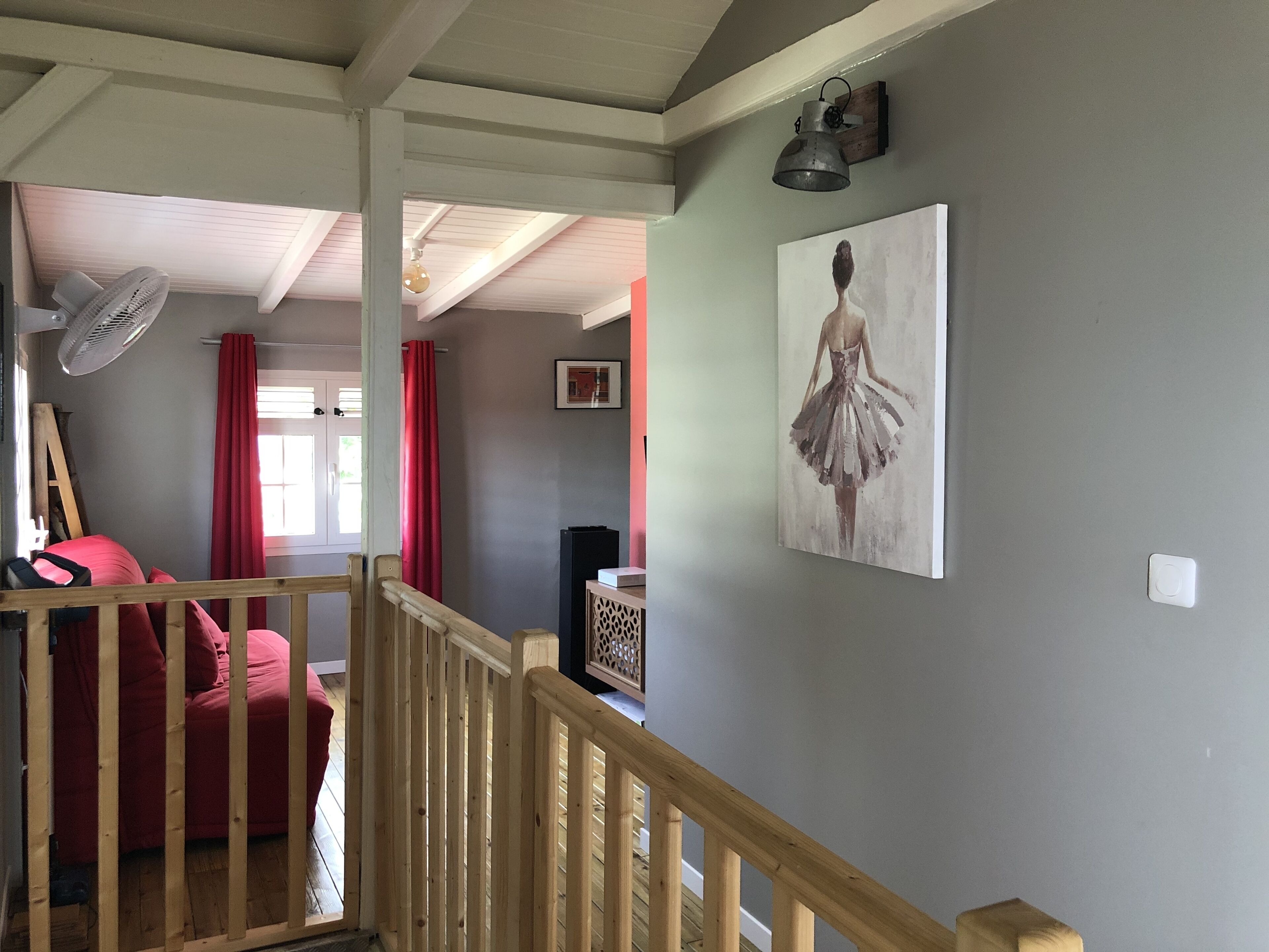 A room with a wooden staircase, a red couch, a painting of a ballerina, and a fan.