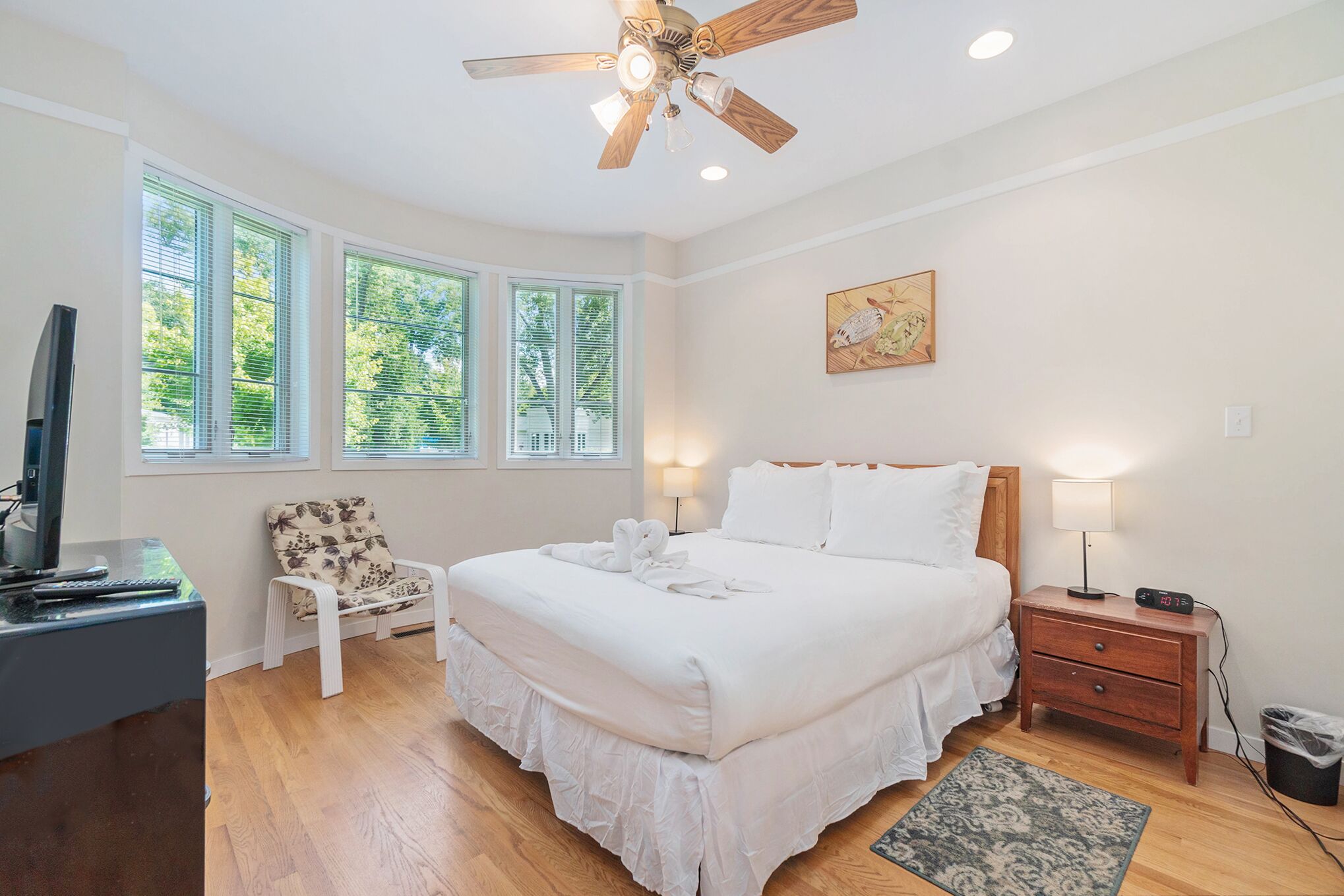 A bedroom with a bed, a desk, a chair, a nightstand, a lamp, and a ceiling fan.