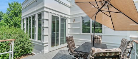 A deck with a table and chairs, a large umbrella, and a white building with glass doors.