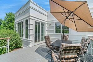 Une terrasse avec une table et des chaises, un grand parasol et un bâtiment blanc doté de portes vitrées.