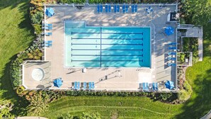 Vista aérea de una piscina con múltiples carriles, rodeada de césped cuidado y protegida por árboles.