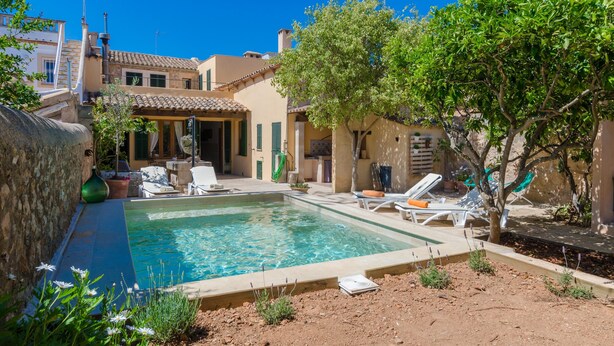 A swimming pool with lounge chairs, a stone wall, and a tree in a residential setting. - CAN MORA - Villa with private pool in Campos. Free WiFi (Campos)