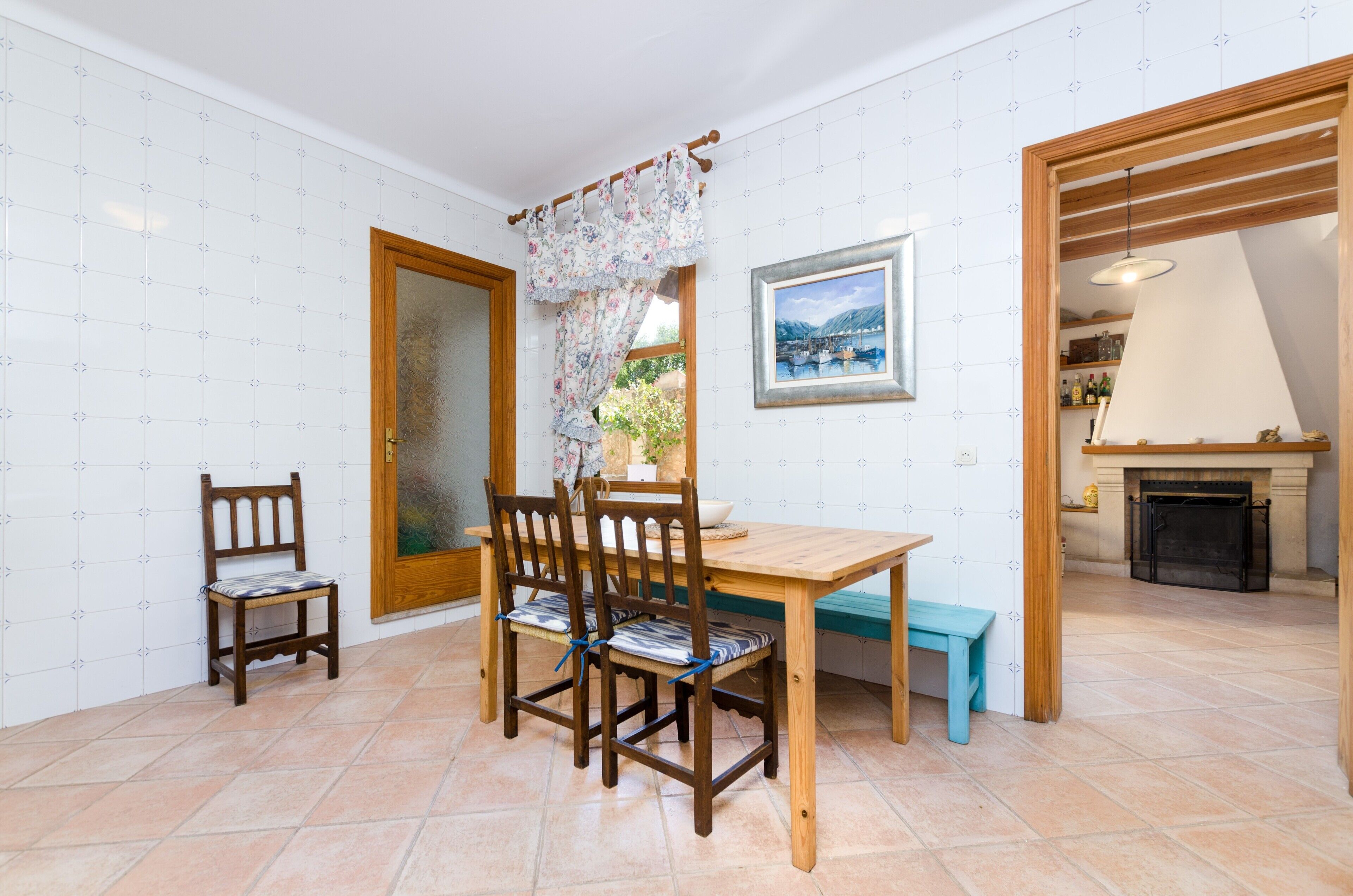 Un comedor con una mesa y sillas de madera, un banco, una chimenea y un cuadro en la pared.